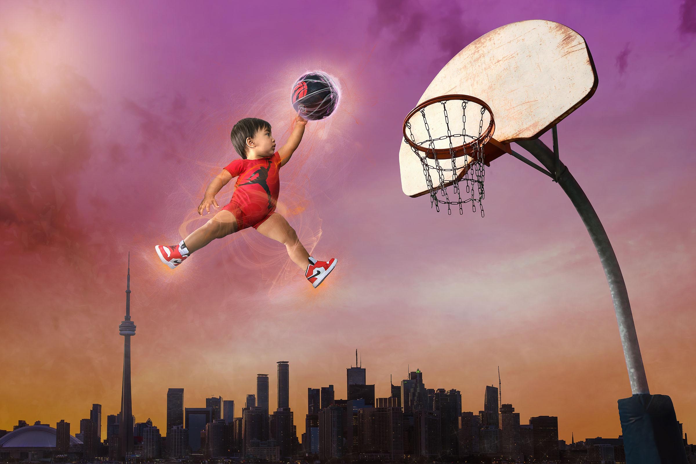Baby boy flying in the air dunking a Toronto Raptors basketball into a hoop with city of Toronto below him composite by Vaudreuil-Soulanges and West Island of Montreal photographer Tobi Malette