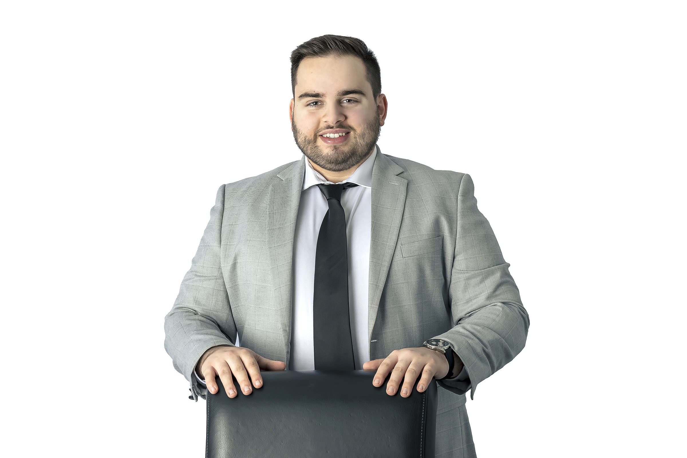 Portrait corporatif homme portant habit gris debout avec les mains sur une chaise en studio fond blanc par Tobi Malette photographe Vaudreuil-Soulanges et ouest de l'ile de montreal