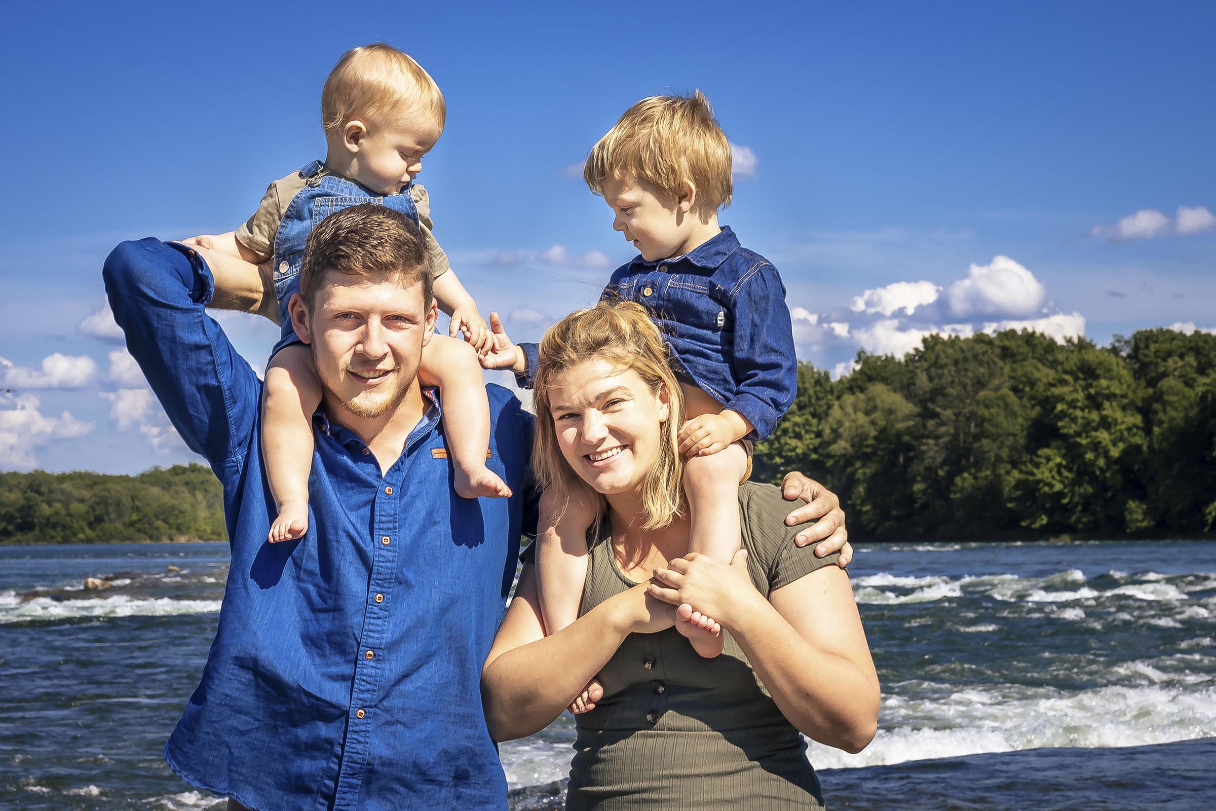Portrait famille avec deux jeunes garçons sur les épaules de leur parents au bord de l'eau par Tobi Malette photographe Vaudreuil-Soulanges et ouest de l'ile de montreal