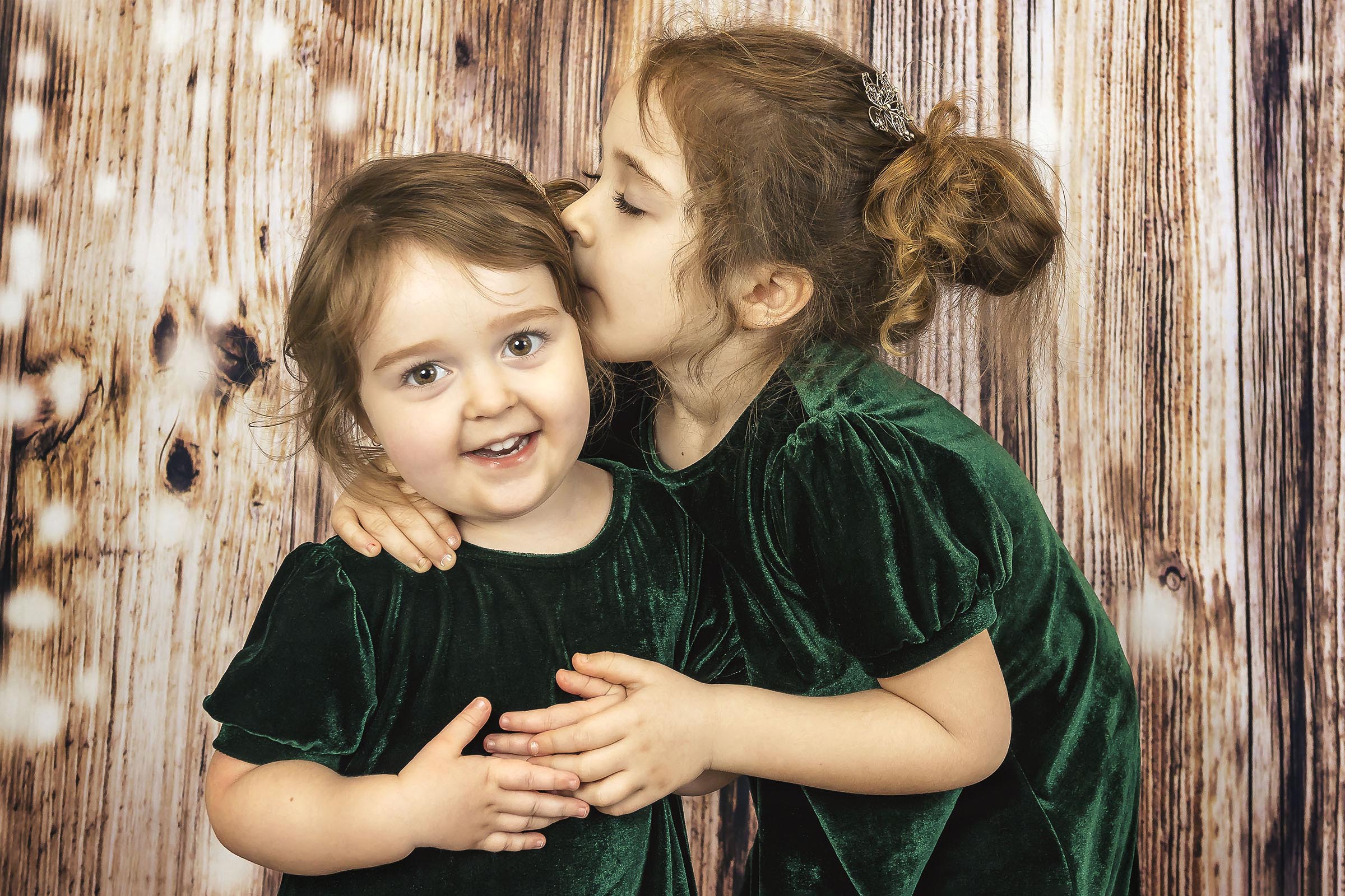 Beaux-arts portrait deux jeunes filles portant robes vertes en velours grande soeur donne bisou surla joue en studio mur bois par Tobi Malette photographe Vaudreuil-Soulanges et ouest de l'ile de montreal